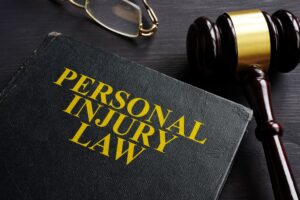 Glasses, gavel, and Personal Injury Law textbook on dark wood surface.