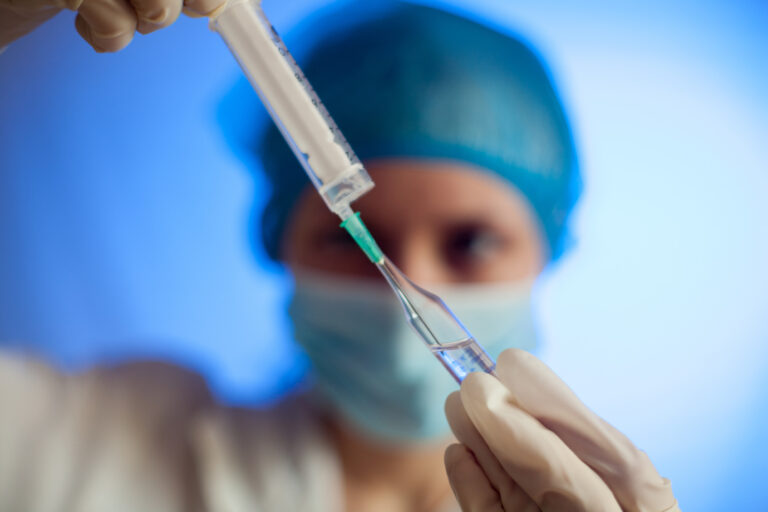 A surgeon in a cap and mask with a test tube and vial.