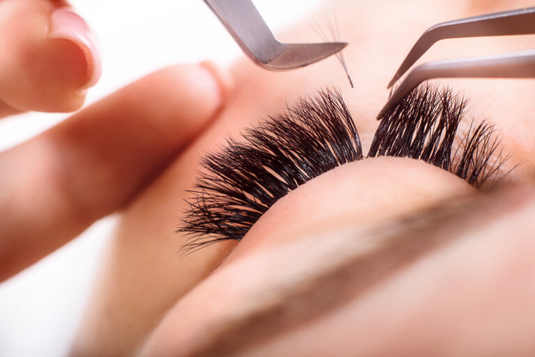 A beautician uses a tool on a woman during lash extension treatment