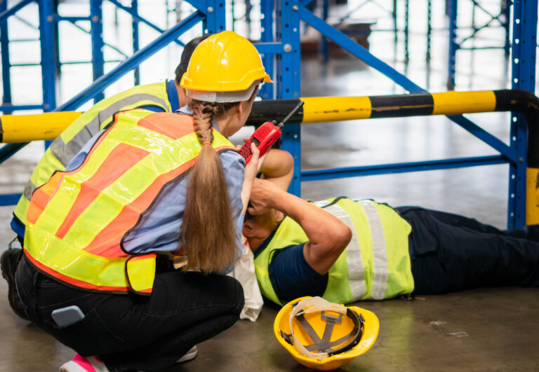 A worker lying on the floor due to inadequate training, another employee kneels over him.