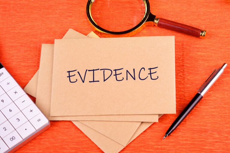 Cards with the word evidence printed on them on an orange background with a magnifying glass and pen.