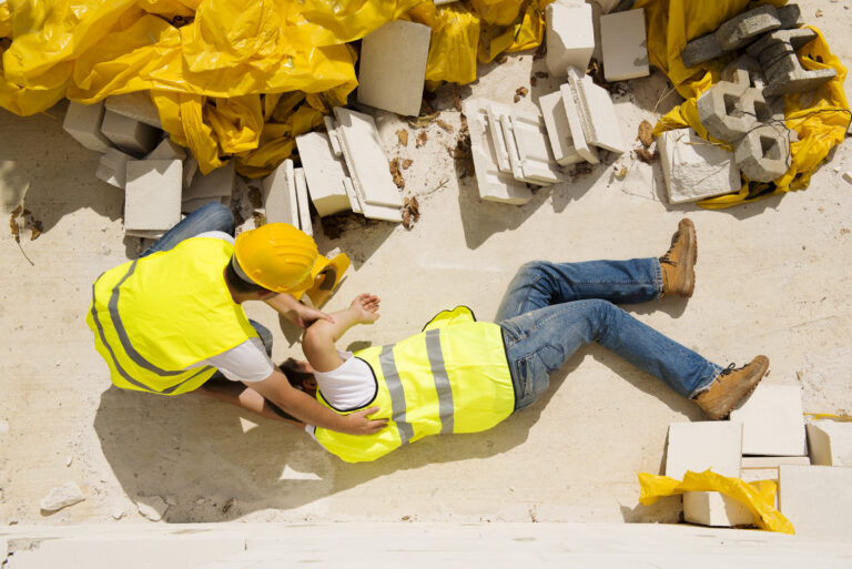 A fallen construction worker is helped by a colleague.
