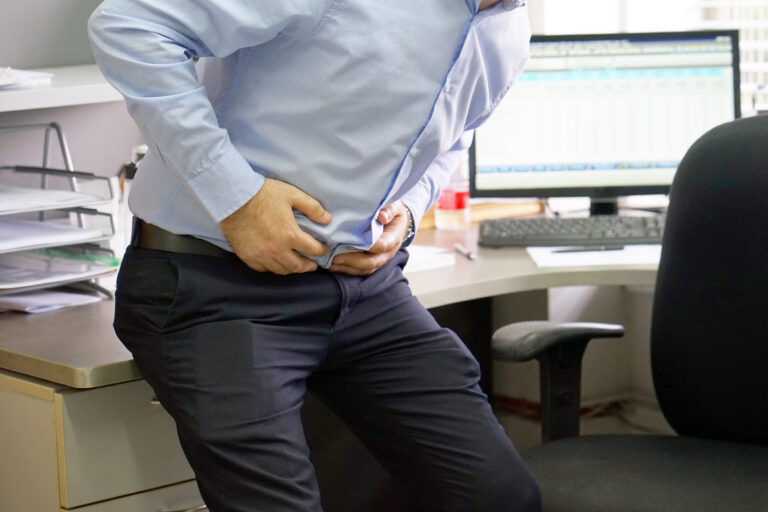 A man sitting on his desk in an office holding his abdomen in pain.